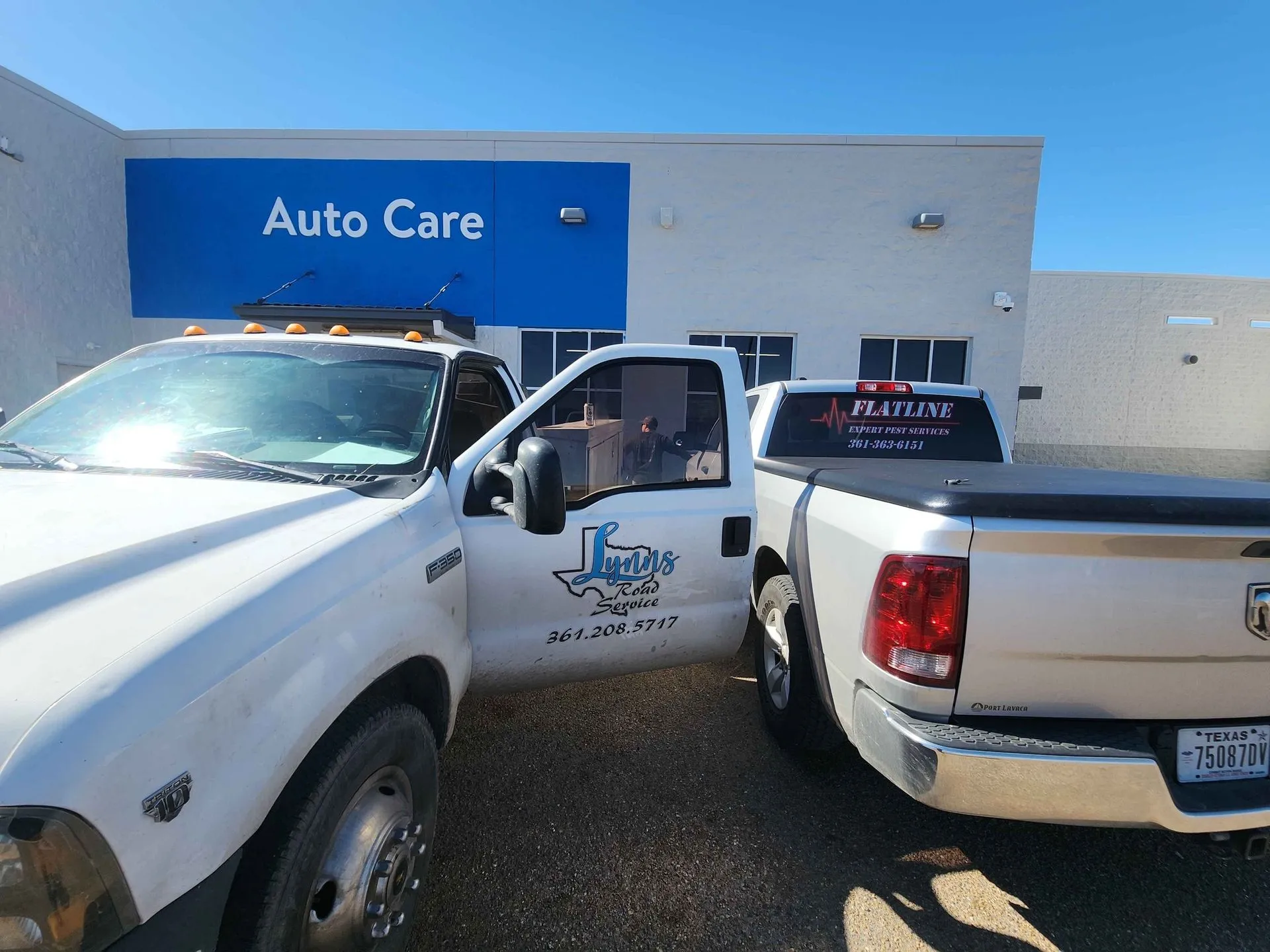 Two white Lynn's Road Service trucks parked outside an auto care building.