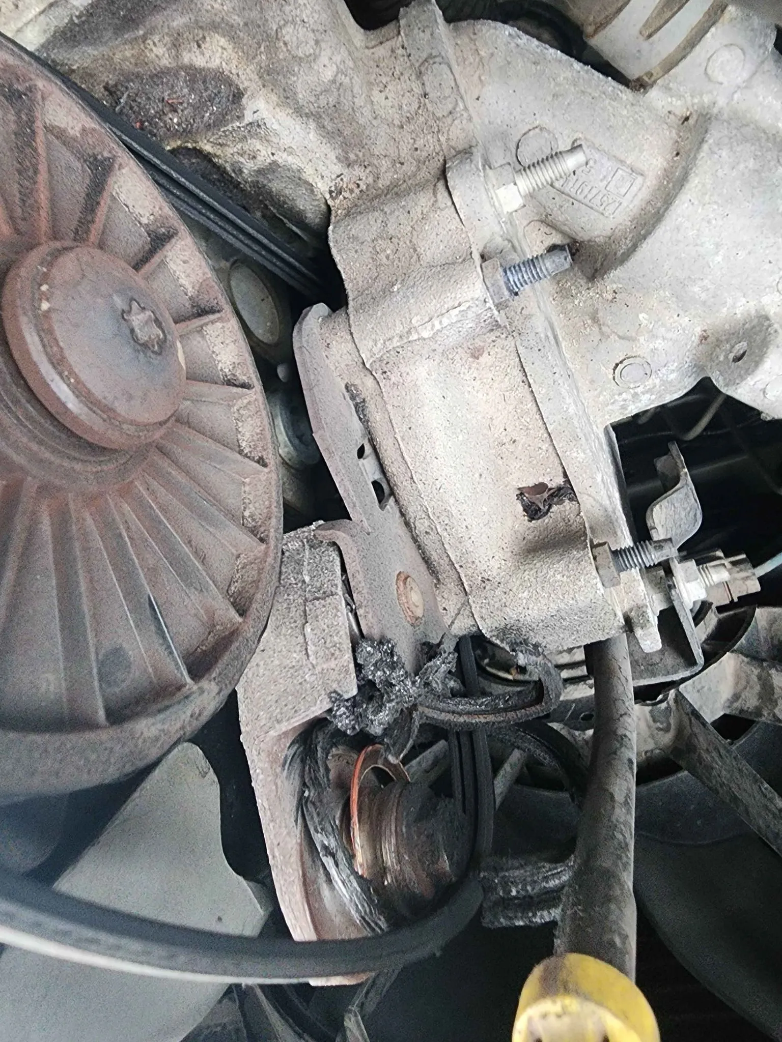 Damaged car alternator with melted components beside a fan and belt.