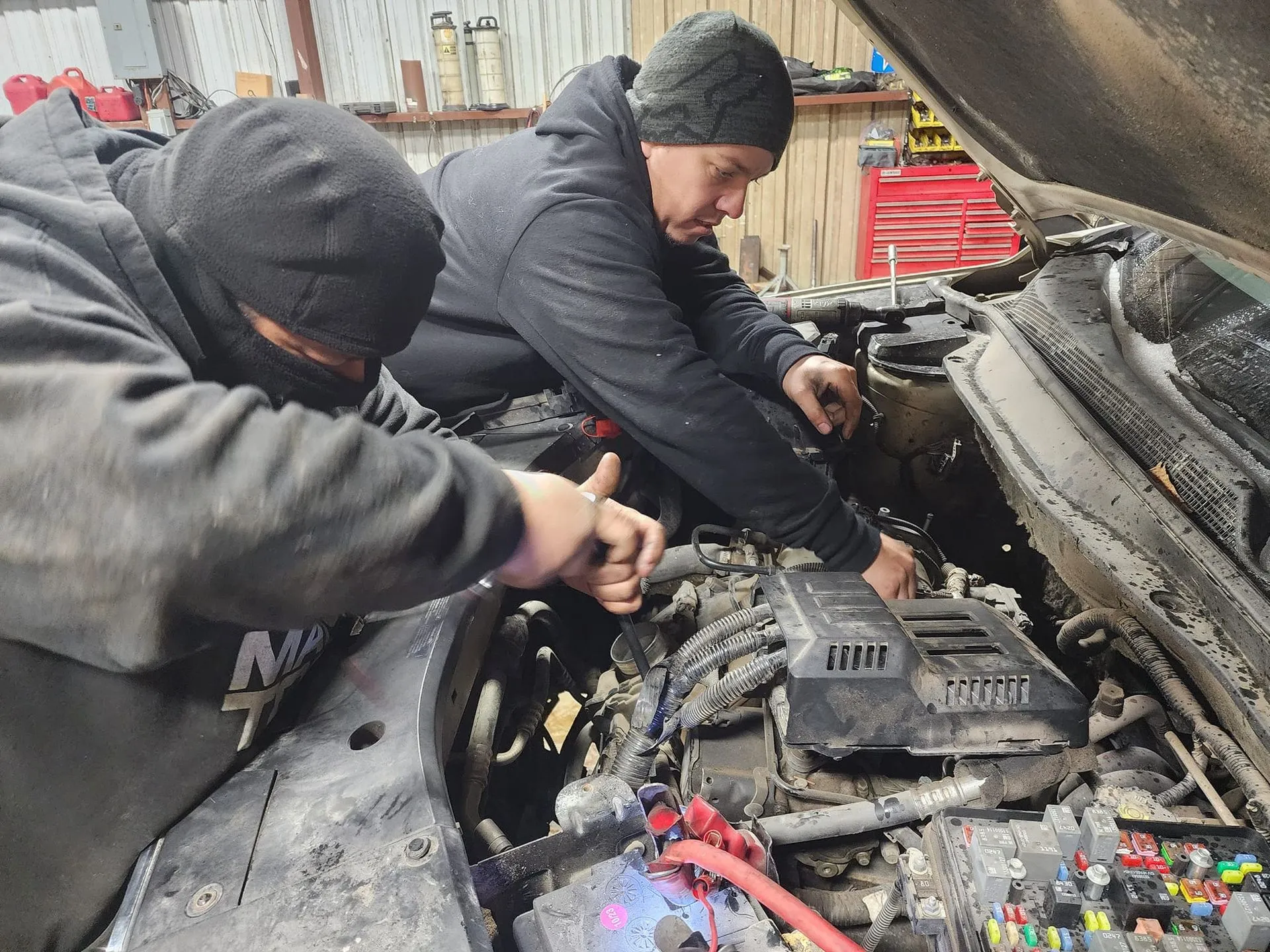 Two mechanics working on a car engine inside a garage.